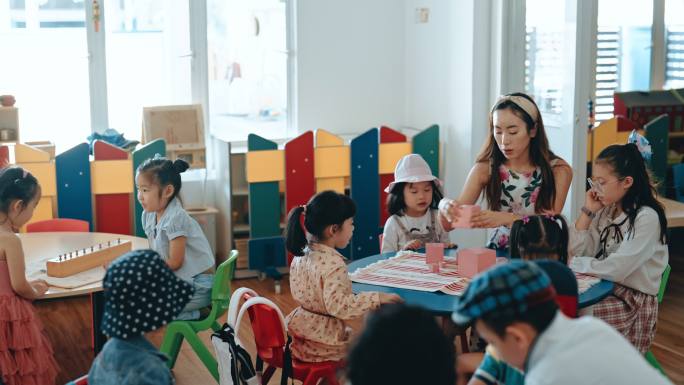 亚裔华裔蒙台梭利幼师在教室里用玩具积木在塔楼上展示学生