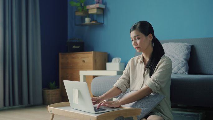 年轻的亚洲女性坐在地板上通过笔记本电脑上网课。