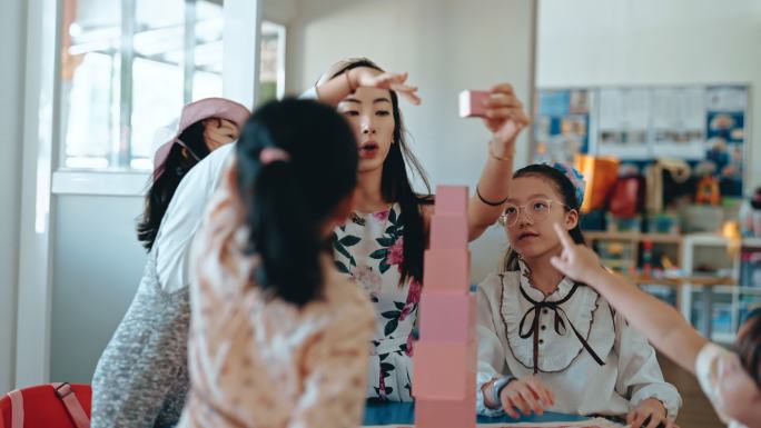 亚裔华裔蒙台梭利幼师在教室里用玩具积木在塔楼上展示学生