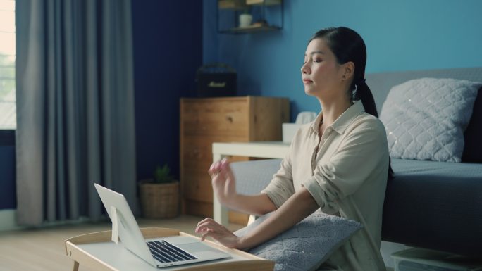 年轻的亚洲女性在家上网学习时患上办公室综合症后伸懒腰。