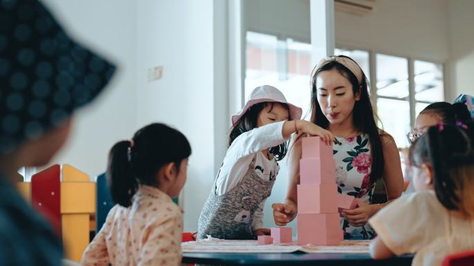 亚裔华裔蒙台梭利幼师在教室里用玩具积木在塔楼上展示学生
