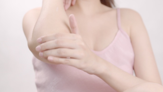 亚洲成年女性用手在手肘和手上涂抹保湿霜。身体护理理念。