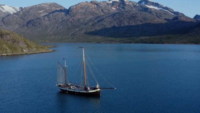 在阳光明媚的蓝海上航行，背景是格陵兰岛的群山