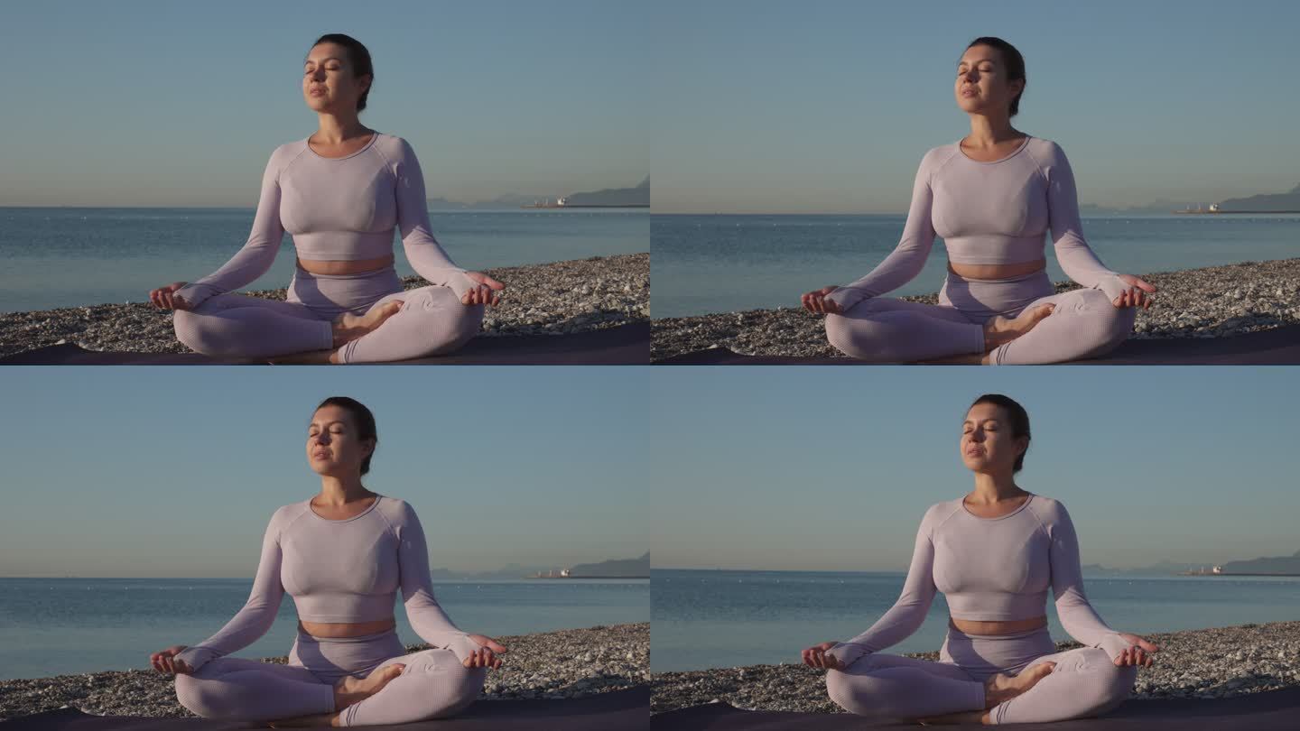 一位健康的年轻女子坐在瑜伽莲花中，闭着眼睛面对大海，日出时在沙滩上冥想。