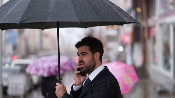 雨中的快乐商人商务人士雨中打伞打电话