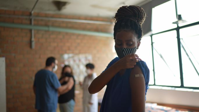 一名年轻女性接种疫苗后展示手臂的肖像-使用口罩