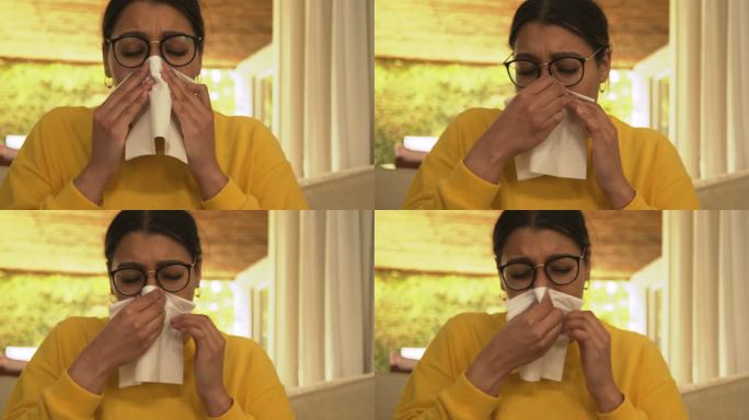 一位年轻女子在家里的沙发上养病时擤鼻涕。女人在休息室的沙发上使用纸巾并感到恶心