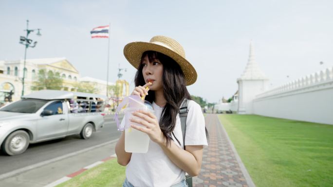 年轻的亚洲女性在曼谷大皇宫旅行时喝着椰子汁