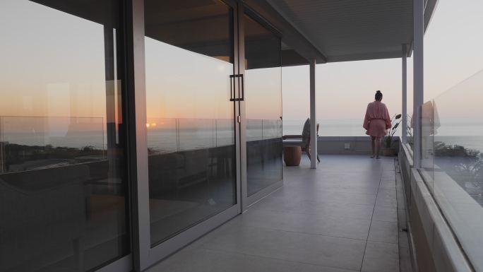 穿着连衣裙的女人走在享有日落海景的豪华阳台上