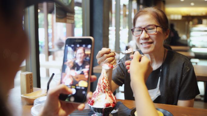 亚洲女人吃着冰糖甜点，满脸笑容地拍照。