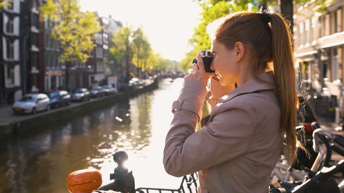 正在阿姆斯特丹旅行的年轻女性，用复古模拟相机拍摄运河，对着相机微笑
