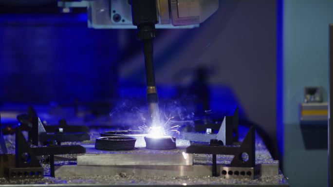 在室内制造设备中，机器人CNC机械臂将一层铝焊接到圆形金属形状上的侧视图
