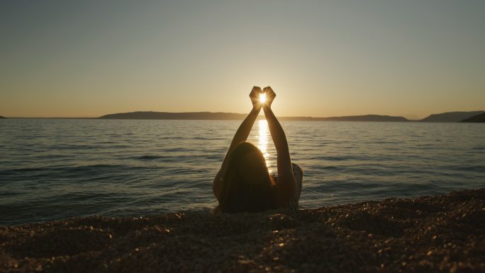 年轻女子躺在沙滩上用手展示心形符号