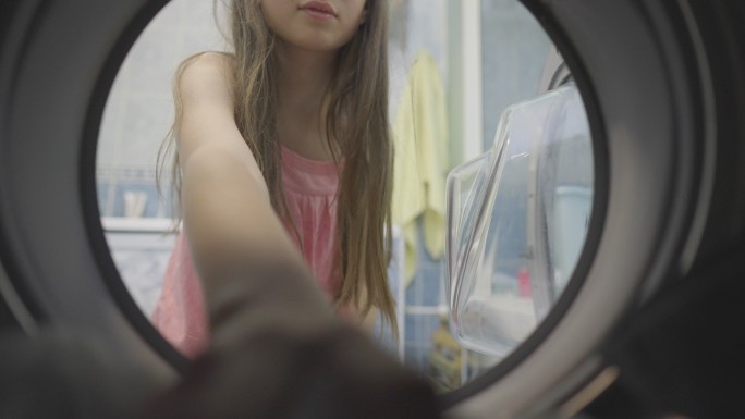 一个戴眼镜、身穿粉色T恤的十几岁女孩从洗衣机里取出干净的衣服。