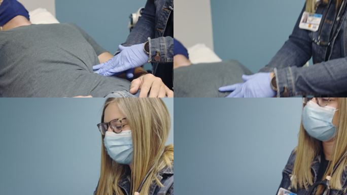 一名年轻的女医生助理（PA）戴着外科口罩和丁腈手套按压着一名40多岁的蒙面白人男性的腹部，该男性躺在