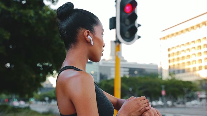 混血女子在户外跑步时用数字手表计时。女运动员戴着健身追踪器在城市慢跑。运动员看着手表戴着耳机
