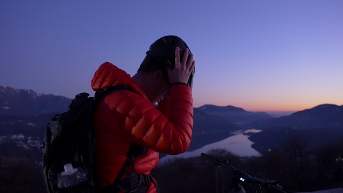骑山地车的人在日落后的蓝色小时放松身心，欣赏下面的湖泊和山脉
