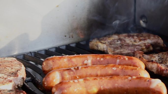 用火焰和烟熏烤牛排的翻肉和热狗。家庭烧烤派对。