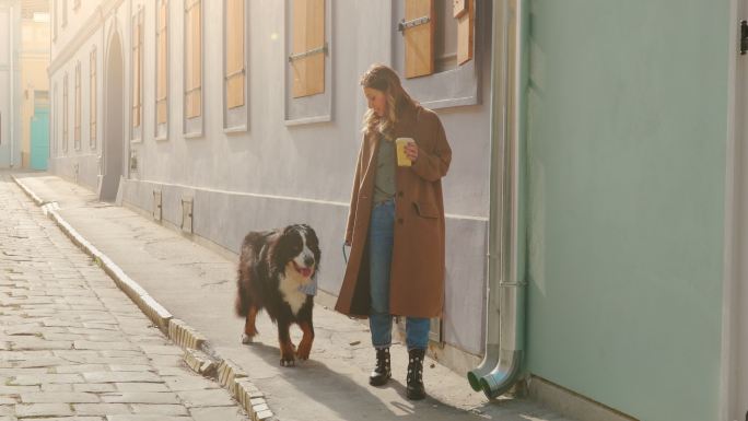 金发女孩拿着咖啡杯，带着狗走在街上