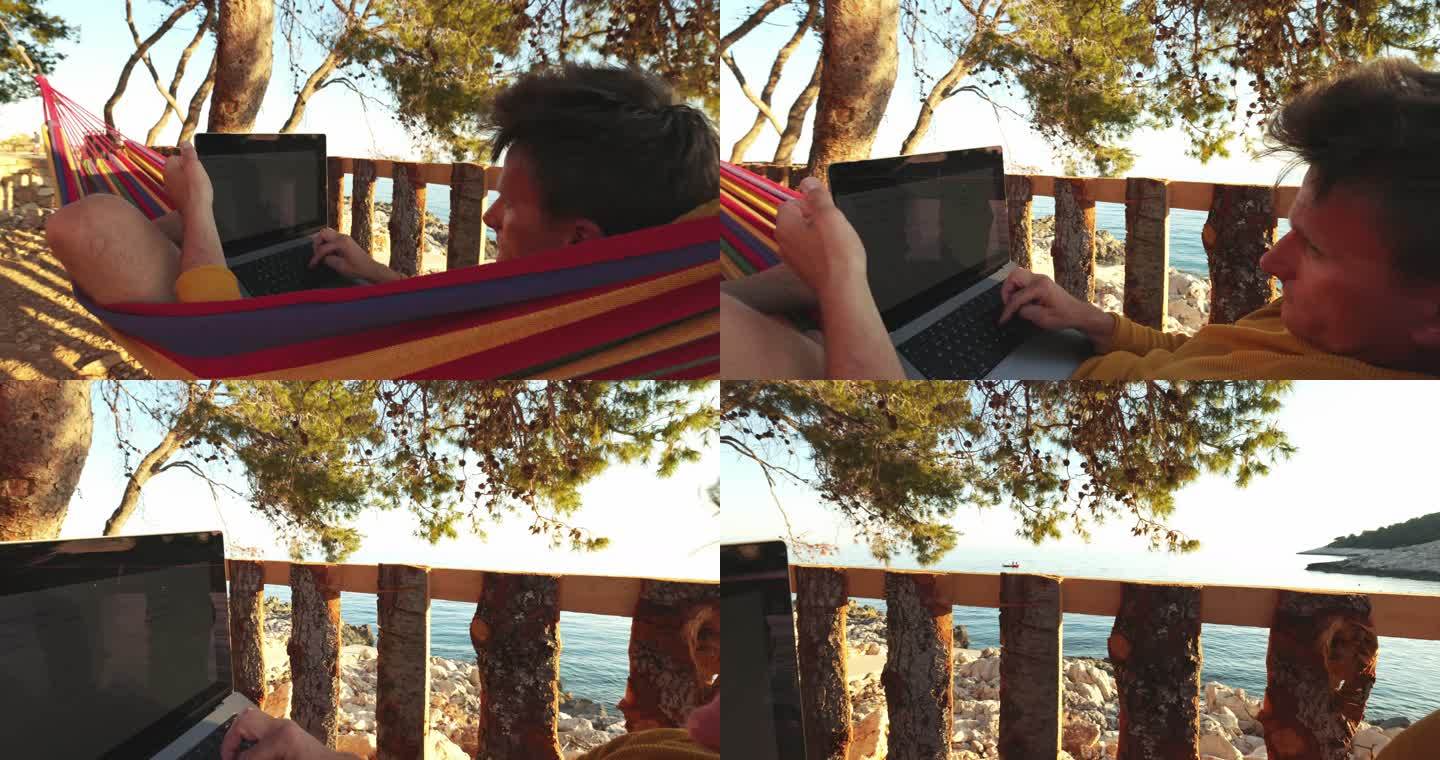 一个棕色短发的男人晚上躺在海边的吊床上用笔记本电脑工作，面包车生活