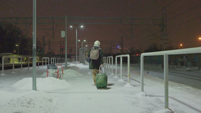 一位带着行李的成熟女性，一位旅游者，在寒冷、雪夜的铁路站台上走着，等待她的火车。