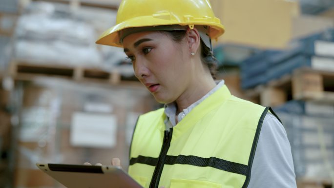 年轻的亚洲仓库检查员使用数字平板电脑检查库存。