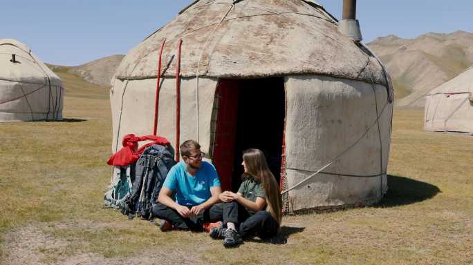 年轻的男女背包客早上在吉尔吉斯斯坦蒙古包营地的山上相遇