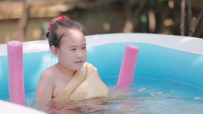 夏季，穿着泰国传统服装的亚洲小女孩在游泳池里玩水枪
