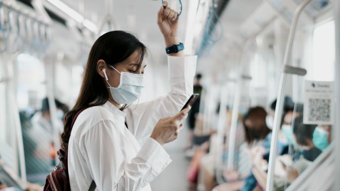 年轻的亚洲女性戴着口罩在地铁打电话