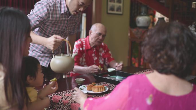 中国儿子在多代人之间喝茶，在下午茶聚会期间在家享用传统中秋月饼和中国茶