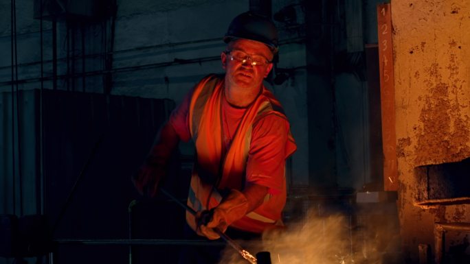 男工人从铸造厂的容器中提取熔融金属样品