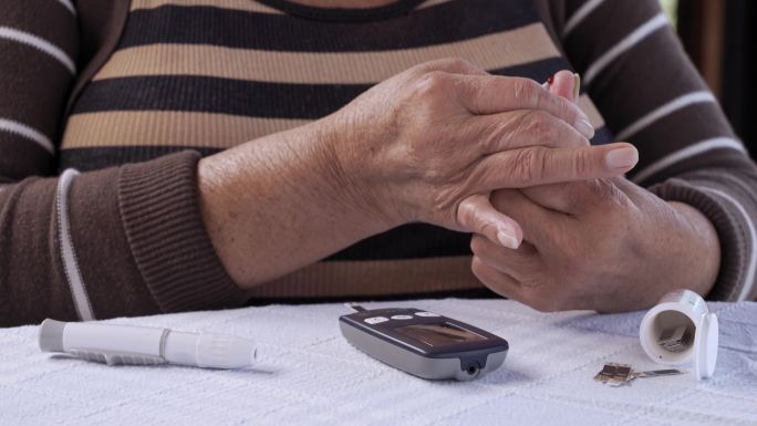 西班牙裔老年妇女用手指上的柳叶刀通过血糖仪检查血糖水平的特写镜头