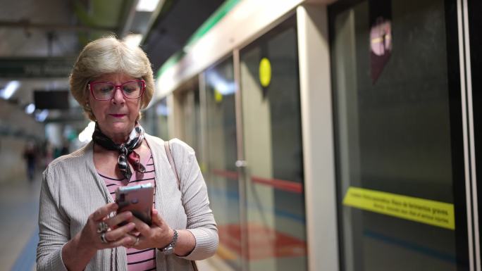 老年女性在等待地铁列车时使用手机