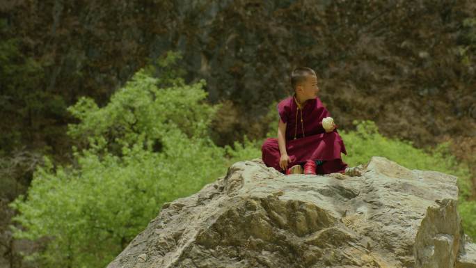 小喇嘛坐在石块上吃馒头