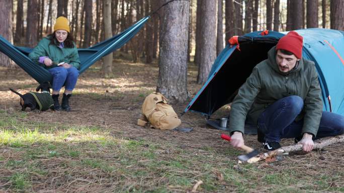 两位千禧一代登山者享受着自然美景。一个女人在和宠物玩，而一个男人在砍柴