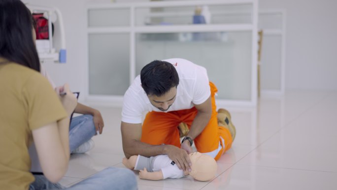 教练对婴儿训练娃娃进行心肺复苏。年轻的男性教练演示如何在一个玩偶假人上进行心肺复苏训练。