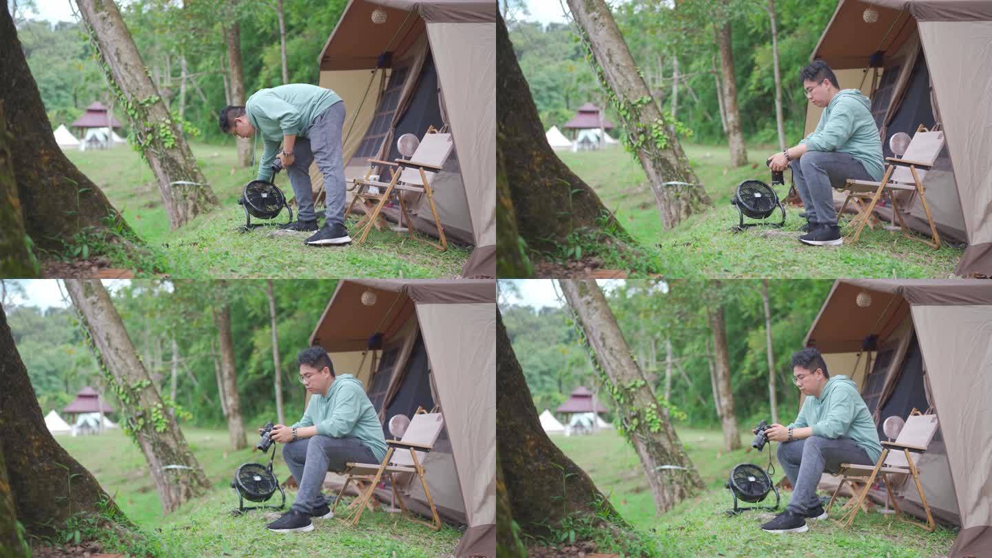 周末休闲活动期间，一名放松的亚洲华裔中年男子在帐篷露营前查看无镜相机