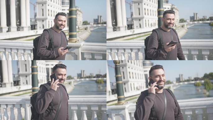 在慢动作视频中，微笑的男性游客在渡河大桥时用智能手机交谈