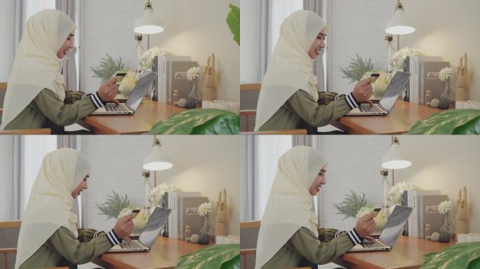 一位身穿宗教服装的年轻漂亮的穆斯林女性正在使用信用卡上网购物，坐在家里客厅的笔记本电脑前。一名伊斯兰