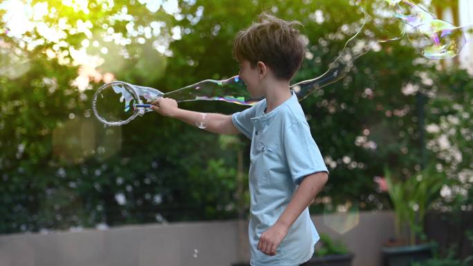 一个小男孩拿着一根巨大的泡泡棒在后花园里玩耍。