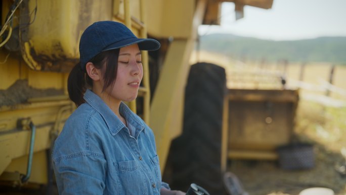 年轻女农民在农田联合收割机阴凉处休息喝水的肖像