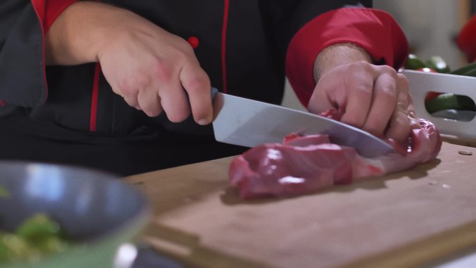 专业厨师在木制案板上将一块生肉切成两半