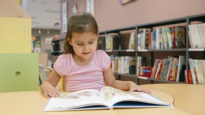 DS小女孩在公共图书馆的儿童桌旁读书