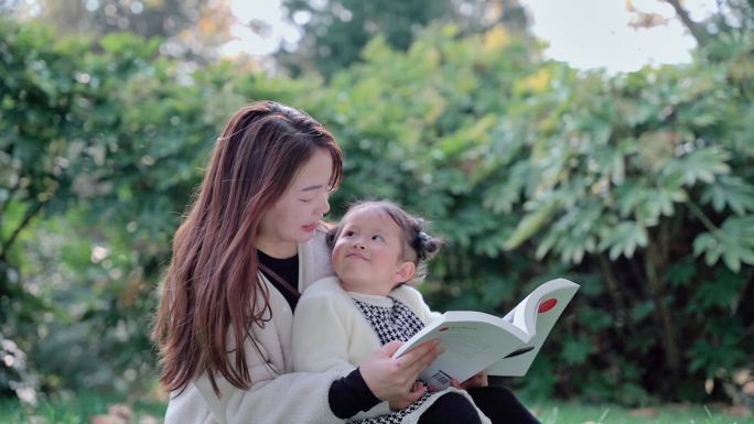 草地上妈妈抱着女儿在亲子阅读