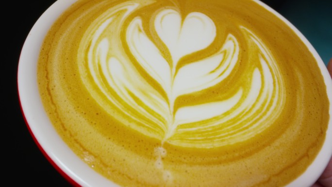 一名咖啡师在咖啡店将蒸牛奶倒入浓缩咖啡杯时制作拿铁咖啡艺术的特写镜头