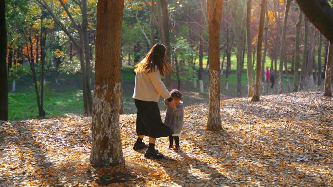 年轻妈妈与女儿在金黄落叶上拉手跳舞