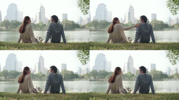 亚洲情侣聊天，坐在绿草上，欣赏美丽的城市景观，人们在城市自然环境中放松身心。