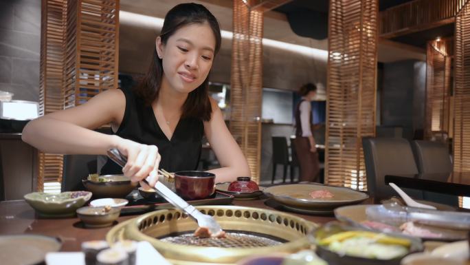 泰国泛亚妇女在餐厅里吃传统的日式牛肉A5烤肉“Yakiniku”，并将生牛肉片放在木炭烤炉上