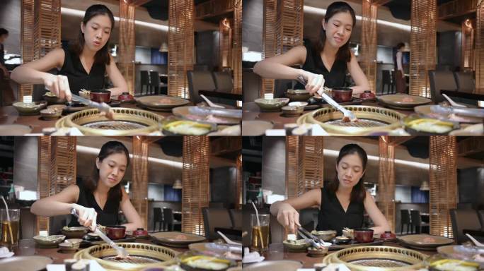 泰国泛亚妇女在餐厅里吃传统的日式牛肉A5烤肉“Yakiniku”，并将生牛肉片放在木炭烤炉上