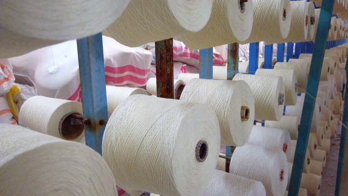 在纺织厂的工业经编机上，白纱卷轴按顺序缠绕筒子线锥